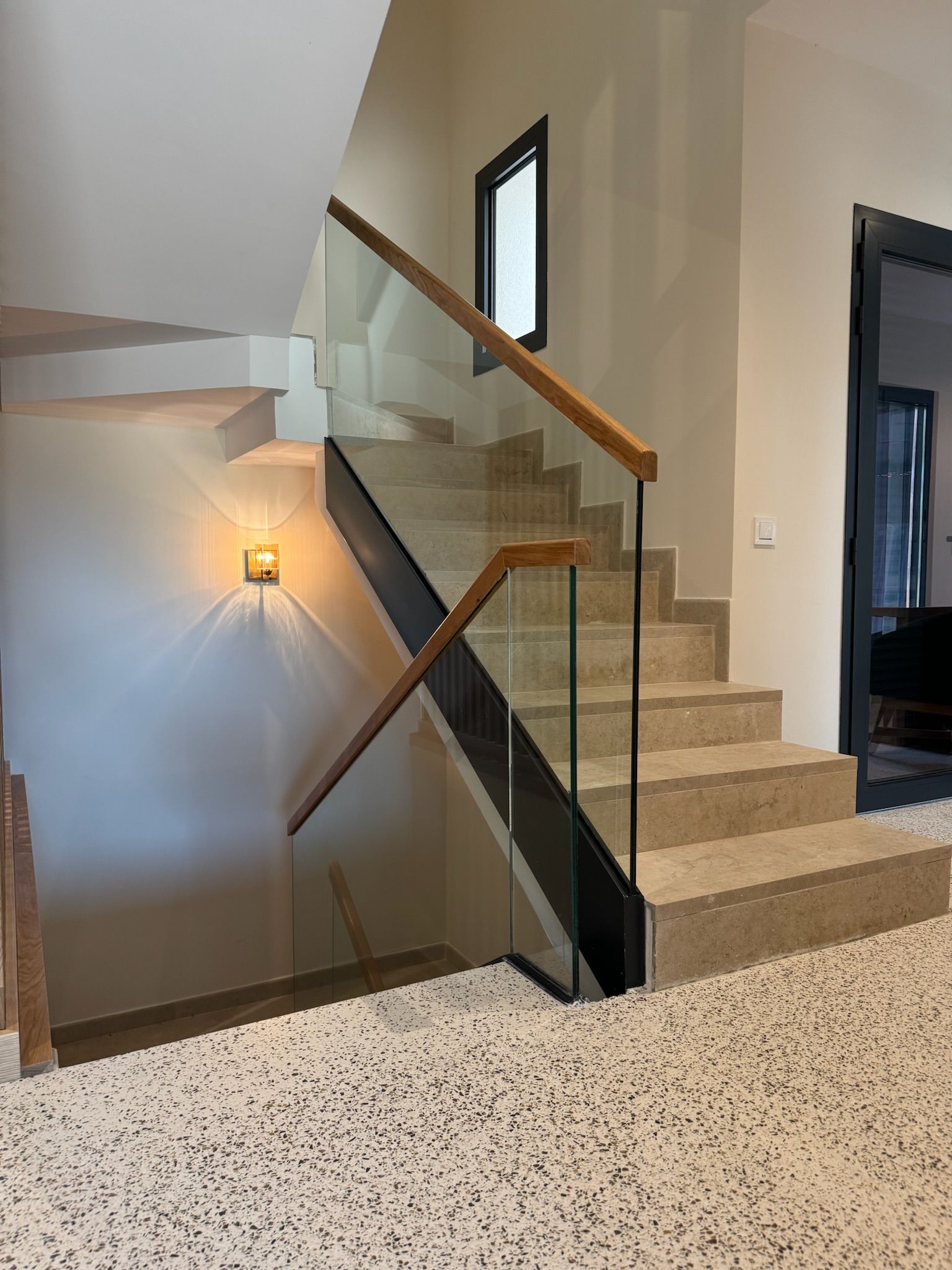 Escalera residencial con Stone Feel cálido, barandilla de cristal y pasamanos de madera