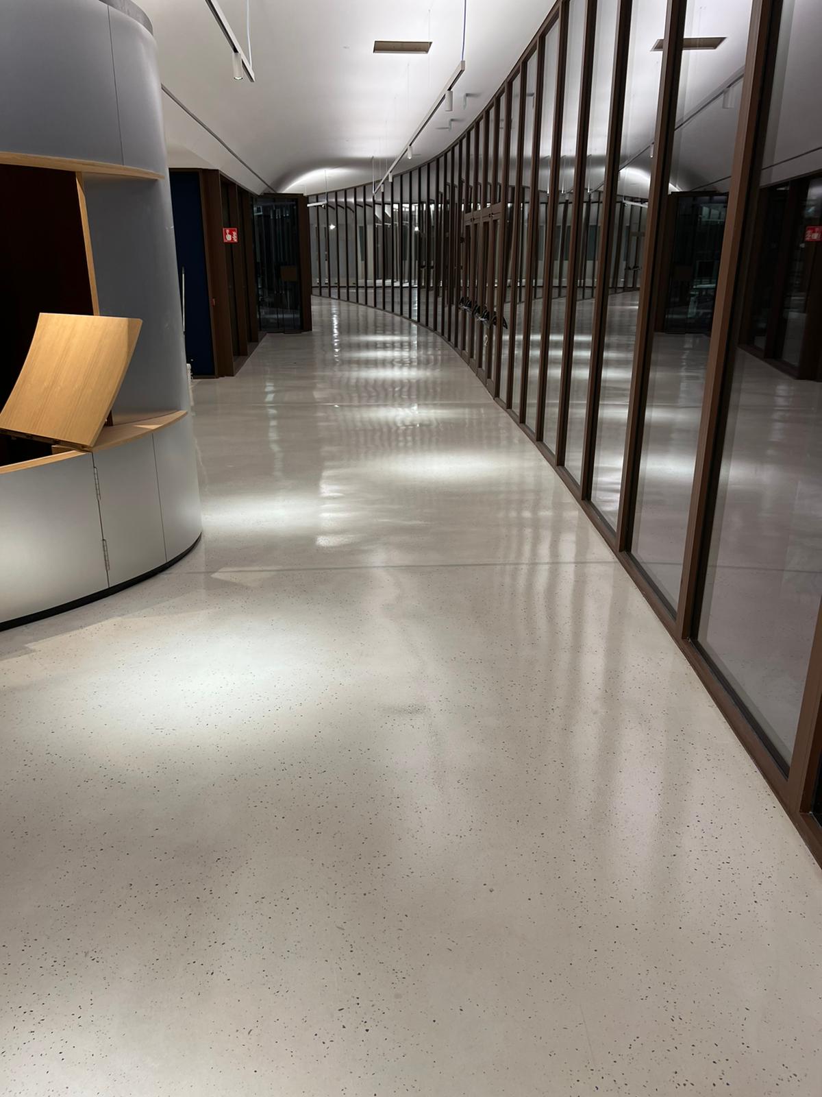 Pasillo curvo Grifols con suelo Stone Feel pulido, cristaleras y mobiliario de madera