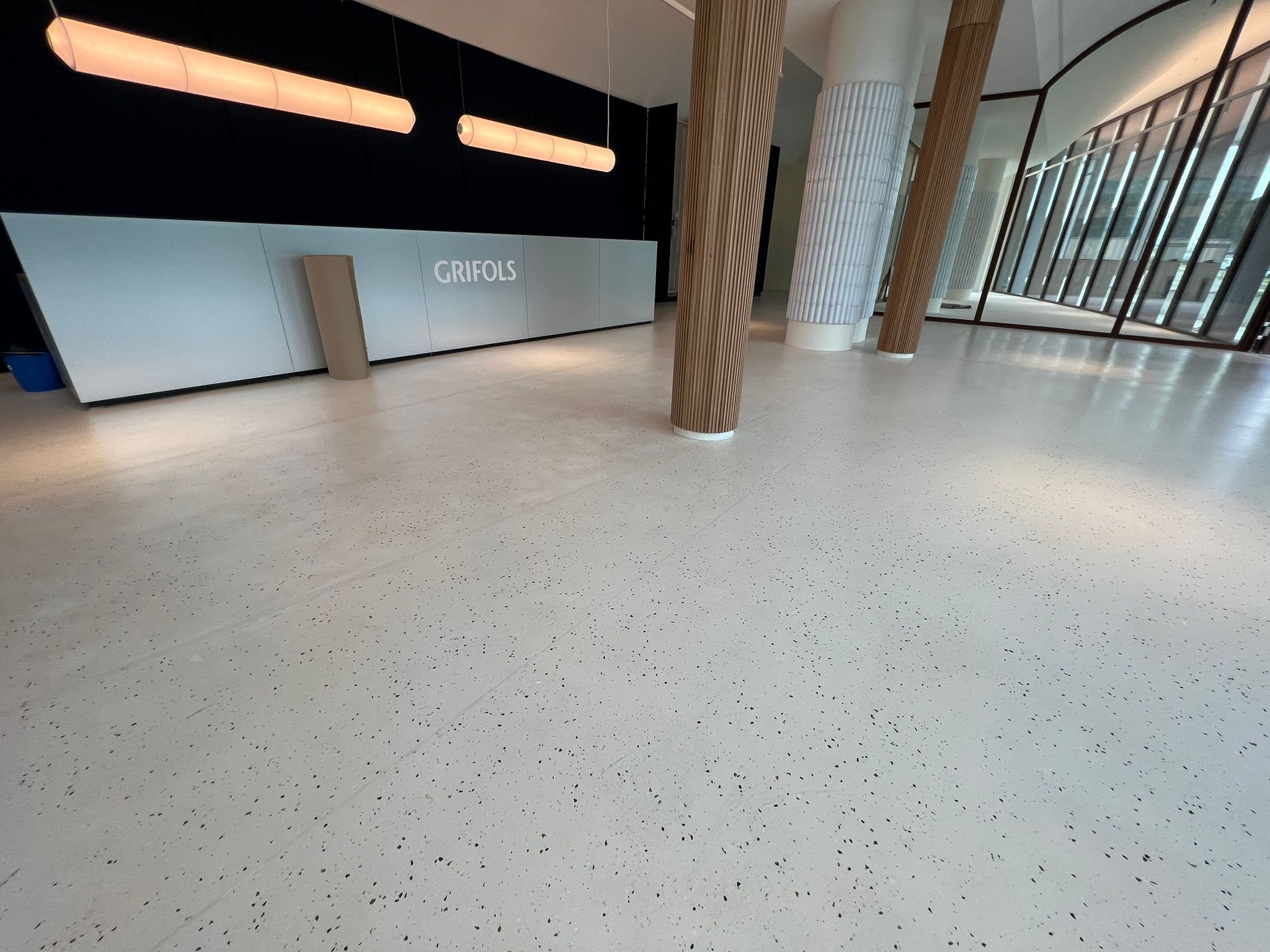 Recepción Grifols con pavimento Stone Feel blanco, columnas de madera y lámparas industriales