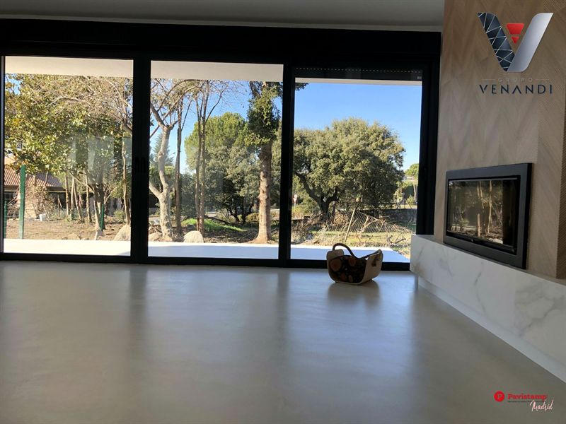 Salón con suelo Decopox gris claro frente a un gran ventanal y una chimenea